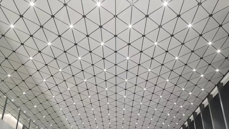 Aluminum ceiling of faceted 3D panels with integrated linear lighting in a public interior